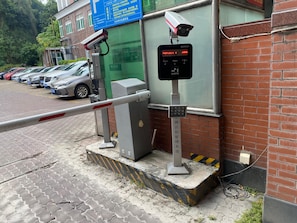 Portilla on vartiointikamera, parkkipaikalla on autoja ja rakennuksessa on sininen kyltti.