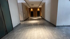 A long, empty hallway with a tiled floor, doors on both sides, and a ceiling with recessed lighting.
