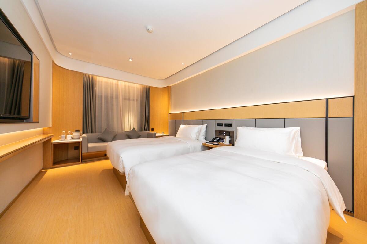 Quarto de hotel com duas camas, televisão, mesa de cabeceira, uma cadeira e cortina.