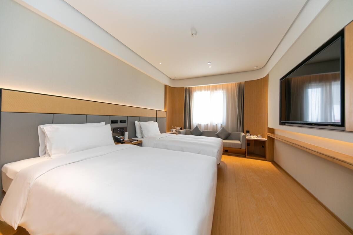 Quarto de hotel com duas camas, televisão, escrivaninha e janela com cortinas.