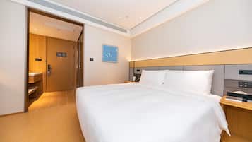 Quarto de hotel com uma cama grande, uma mesa de cabeceira, um criado-mudo, um telefone fixado na parede e uma porta que dá para o banheiro.