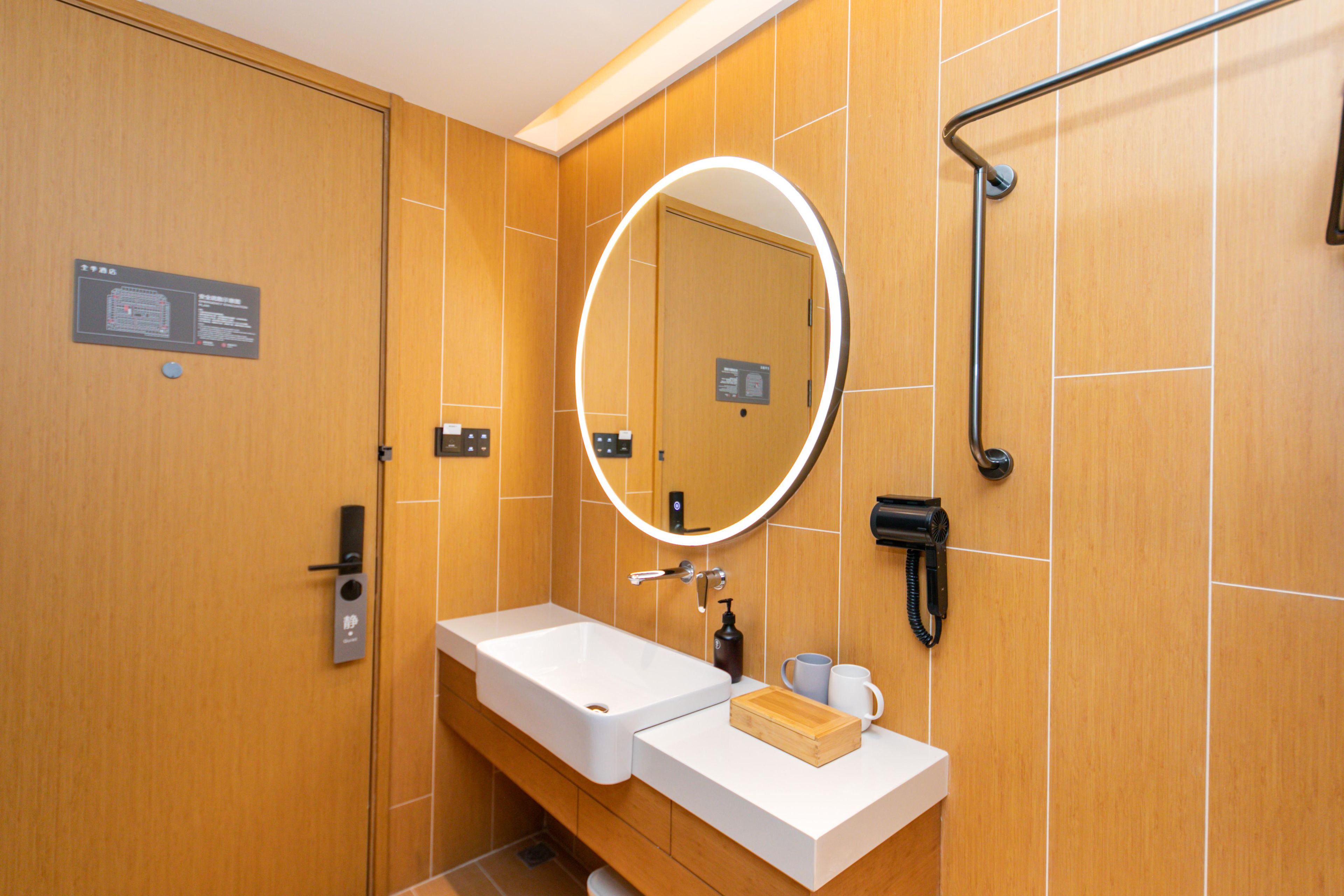 Une salle de bain moderne avec un meuble-lavabo en bois, un grand miroir avec éclairage intégré, une douchette à main et un panneau indiquant les instructions.