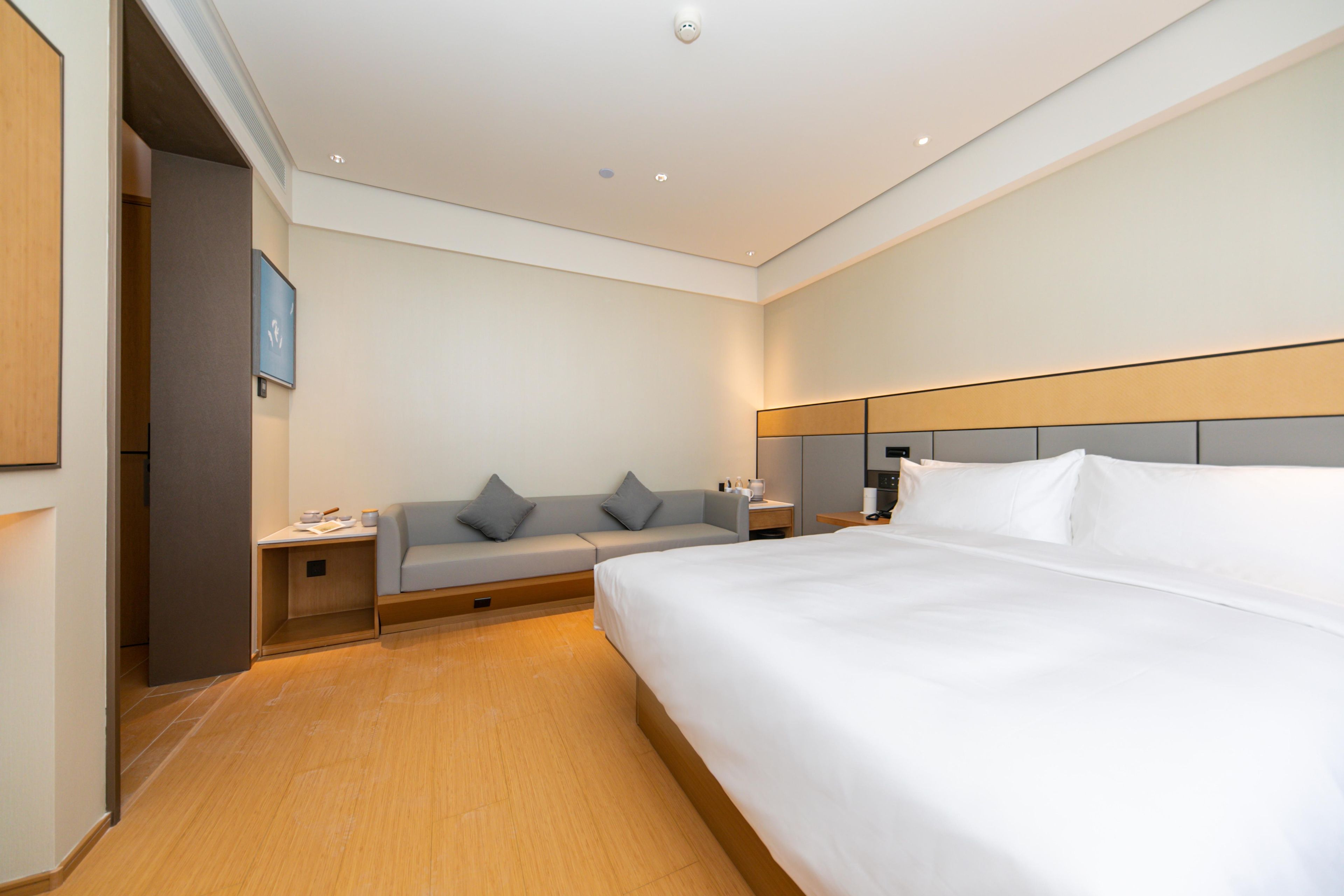 A hotel room with a large bed, a sofa, a bedside table, and a nightstand.