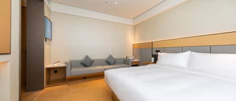 A hotel room with a large bed, a sofa, a bedside table, and a nightstand.