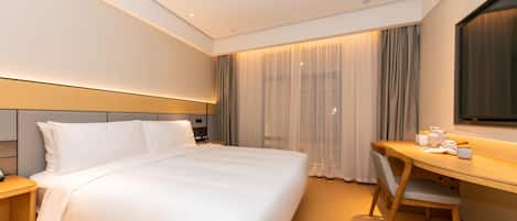 Habitación de hotel con cama, escritorio, silla, mesita de noche y un amplio ventanal con cortinas.
