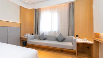 Una habitación de hotel con cama, sofá, una mesita con lámpara y ventana con cortinas.