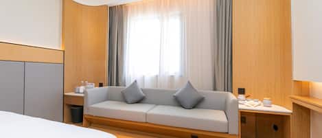 A hotel room with a bed, a sofa, a small table with a lamp, and a window with curtains.