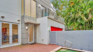 Un edificio moderno con piscina, una puerta de garaje roja y un balcón con plantas.