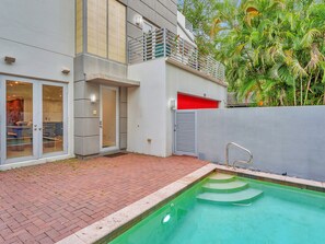 Un edificio moderno con piscina, una puerta de garaje roja y un balcón con plantas.