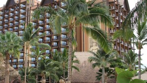 Un hotel con varios balcones, palmeras y zonas de estar al aire libre.