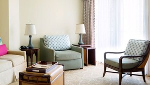 Una habitación de hotel con un sillón verde, una silla de madera, un sofá beige y una pequeña mesa con una lámpara.