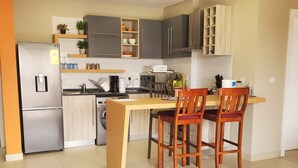 Een moderne keuken met een centraal eiland, houten stoelen en een koelkast.