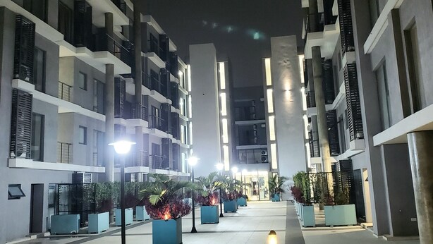 Een modern stadscomplex met meerdere verdiepingen, grote ramen en een centraal open gebied met potplanten en lantaarns.