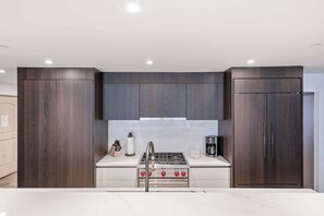 A modern kitchen with dark wood cabinets, a white countertop, stainless steel appliances, and a built-in gas stove. - Village Center C2J - 2 Bedroom Residence (vail)