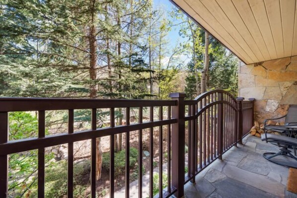 A balcony with a stone wall and a metal railing overlooking a forested area. - Village Center C2J - 2 Bedroom Residence (vail)