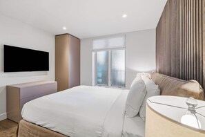 A modern bedroom with a bed, bedside table, and a TV mounted on the wall. - Village Center C2J - 2 Bedroom Residence (vail)
