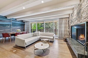 A modern living room with a sectional sofa, a round coffee table, a dining area with a table and chairs, and a fireplace. - Village Center C2J - 2 Bedroom Residence (vail)