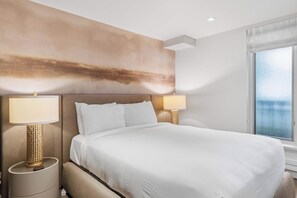 A hotel room with a large bed, two bedside lamps, a wall art piece, and a window with a view.
