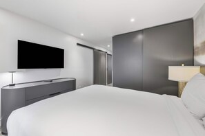 A modern bedroom with a large bed, a flat-screen TV mounted on the wall, a bedside table with a lamp, and a wardrobe with a sliding door. - Village Center C2J - 2 Bedroom Residence (vail)