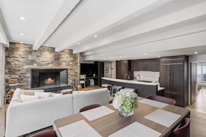 Een moderne woonruimte met een stenen openhaard, een eethoek met een tafel en stoelen, en een keuken met donkere kastjes.