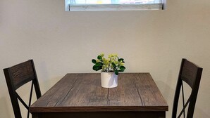 Uma mesa de jantar com quatro cadeiras, um vaso de planta e uma janela com persianas.