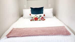 Uma cama bem arrumada com um travesseiro floral, um travesseiro azul e um cobertor rosa.