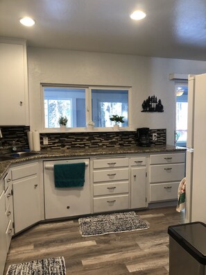 A modern kitchen with white cabinets, a granite countertop, a window with a view, and a black trash bin.