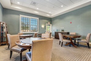 A conference room with round tables and chairs, a bookshelf, and a window with blinds.