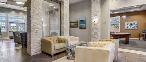 Um hall com um pilar de pedra, sofás bege, mesa de bilhar e mesa de sinuca.