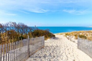 A sandy beach path with wooden fences on both sides, leading to the ocean.