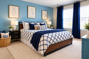 A bedroom with a bed, nightstands, a wicker chair, and artwork on the wall.