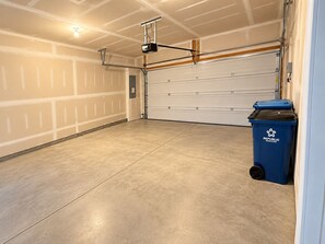 A garage with a closed garage door, a ceiling-mounted projector, and a blue recycling bin. - Family Retreat • King & Bunk Beds • Sleeps 10 (Ocean View)