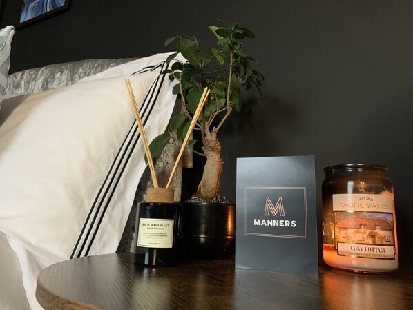 A room with a plant, a diffuser, a candle, and a card on a table.