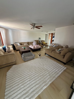 A living room with a large white rug, beige sofas, a coffee table, and a ceiling fan.