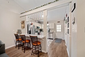 Une cuisine moderne avec des meubles blancs, un plan de travail en marbre et un coin repas doté de chaises en bois.