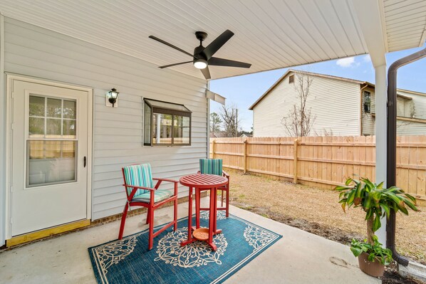 Un patio couvert avec un ventilateur de plafond, deux chaises, une table et un tapis décoratif.