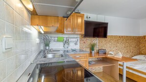 A compact kitchen with wooden cabinets, a built-in stove, and a small dining area with a bed.