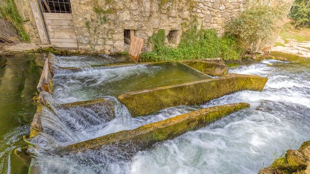 A stone structure with water flowing over it, surrounded by greenery.