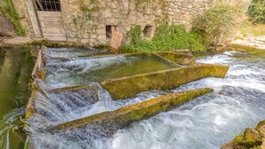 A stone structure with water flowing over it, surrounded by greenery.