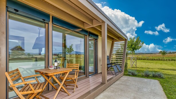 A modern building with large glass windows, a wooden deck, and a view of a green landscape.