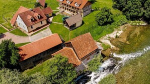 A large, multi-story building with a red-tiled roof, surrounded by lush greenery and a flowing river.