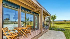 A modern outdoor patio with a wooden table and chairs, large sliding glass doors, and a view of a green landscape.