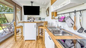 A modern kitchen with a central island, wooden chairs, a built-in TV, and a large window overlooking a deck.