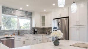 Una cocina moderna con armarios blancos, un refrigerador de acero inoxidable y una isla grande con un florero.