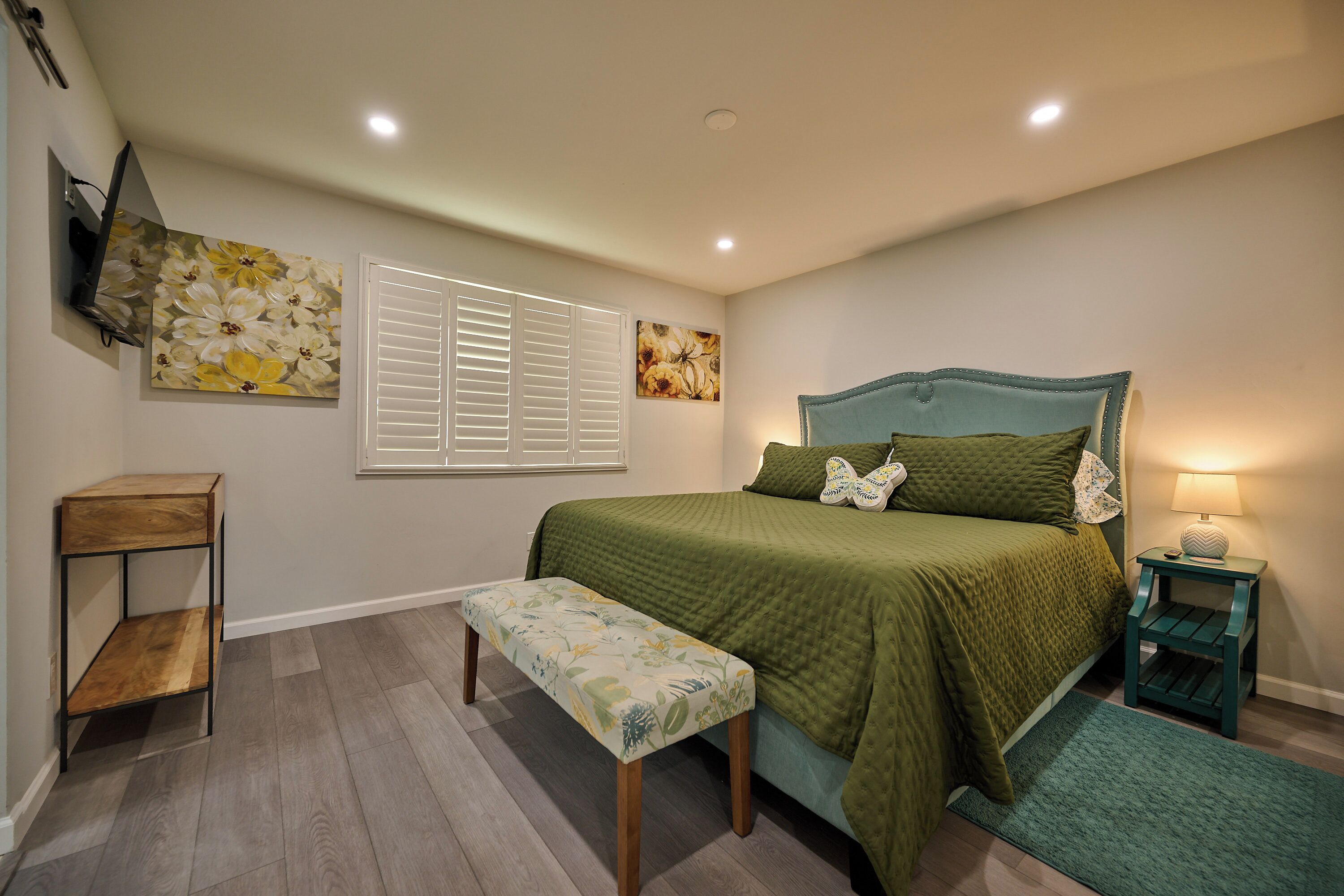 A bedroom with a bed, bench, bedside table, and wall art.