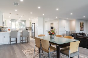 Una cucina moderna con mobili bianchi, un frigorifero in acciaio inossidabile e un'area pranzo con tavolo e sedie in vetro.