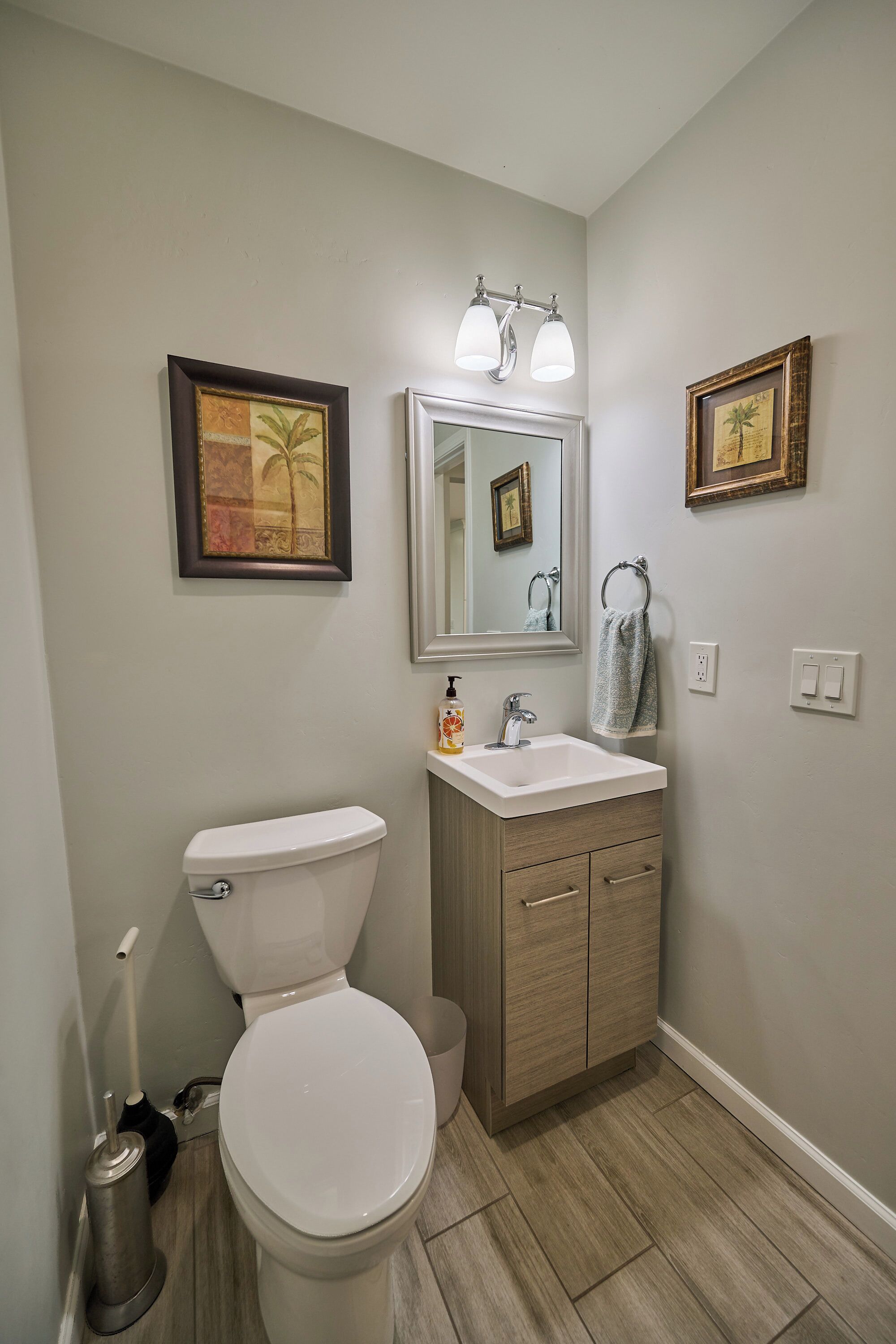 Une salle de bain avec des toilettes, un lavabo et un miroir. Deux tableaux encadrés sont accrochés au mur.