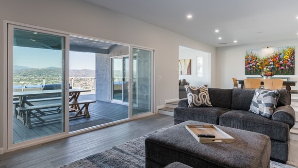 Una sala de estar moderna con un amplio ventanal corredero que da a un patio exterior, un sofá gris y una mesa de madera.