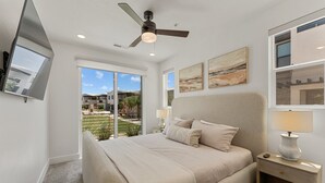A bedroom with a bed, a nightstand with a lamp, a ceiling fan, and artwork on the walls. - Famcation Station #88 (St. George)