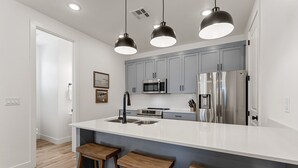 A modern kitchen with a large island, stainless steel appliances, and wooden bar stools. - Famcation Station #88 (St. George)